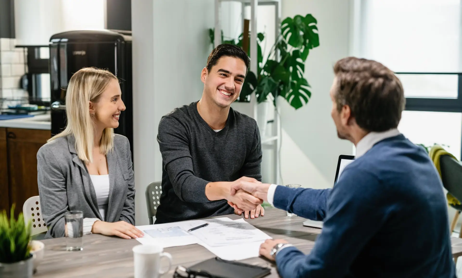 Young happy couple making an agreement with their financial advisor at home men are shaking hands